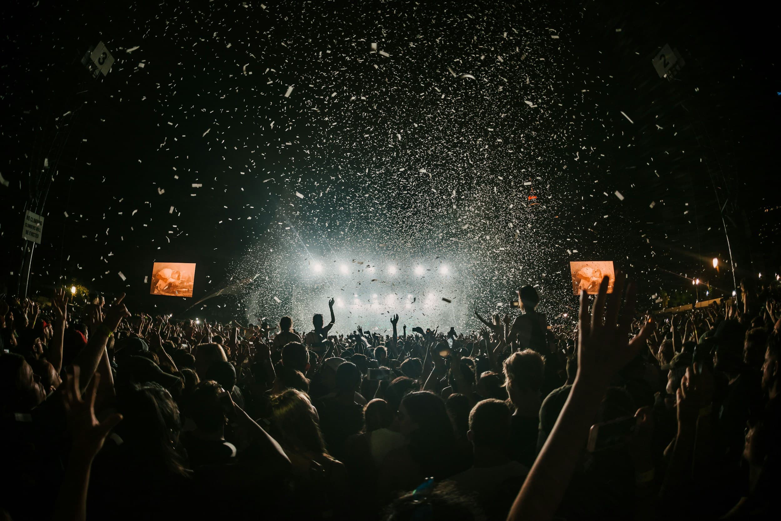 A crowd at a night event, arms raised, confetti falling